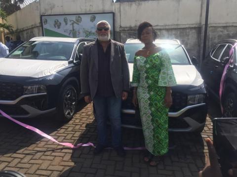 First lady and the donor pose for a photo with vehicles in the background First lady and the donor pose for a photo with vehicles in the background